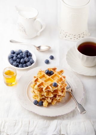 Fresh waffles with blueberries and pouring honey, maple syrup on a white background.の写真素材
