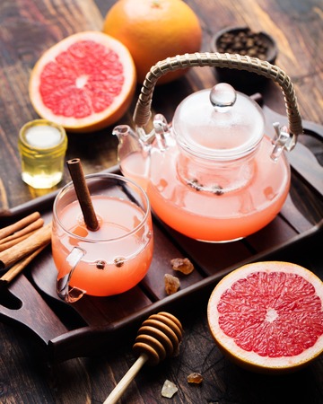 Grapefruit herbal tea with spices and honey in a glass teapot and cup on a dark wooden backgroundの写真素材