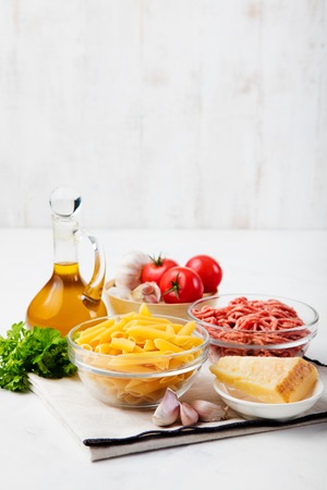 Italian food ingredients: pasta, tomatoes, herbs, minced and spices on wooden backgroundの写真素材