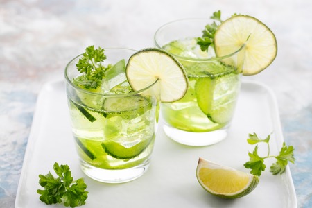 Lime, cucumber, parsley cocktail, lemonade, detox water with ice cubes in a glasses on a white plateの写真素材