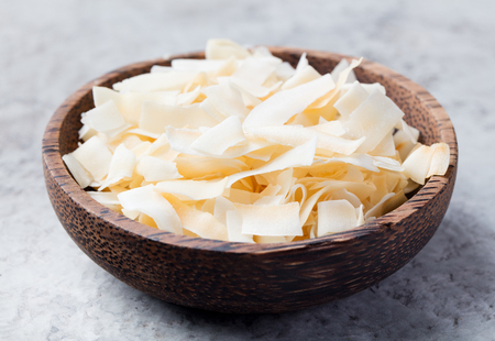 Organic Roasted Coconut Chips Flakes with Sugar and Salt Wooden bowl Stone backgroundの写真素材