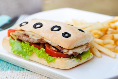 Ciabatta sandwich with grilled beef, tomatoes, cheese and lettuce with french fries on white plate Summer backgroundの写真素材