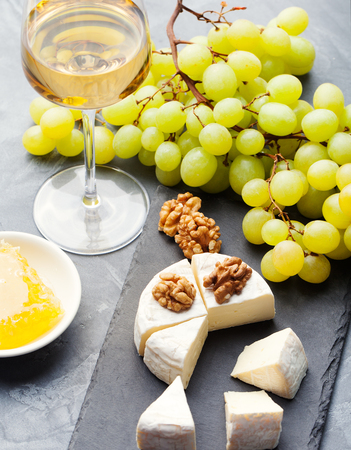 Glass of white wine and assorted cheese with grape on a stone and slate background Copy spaceの写真素材