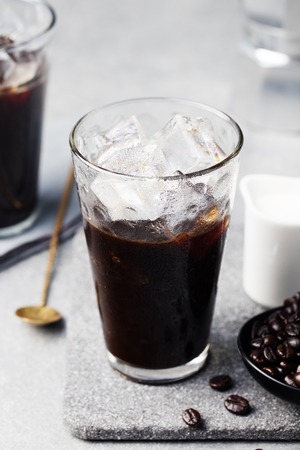 Ice coffee in a tall glass and coffee beans on a grey stone backgroundの写真素材