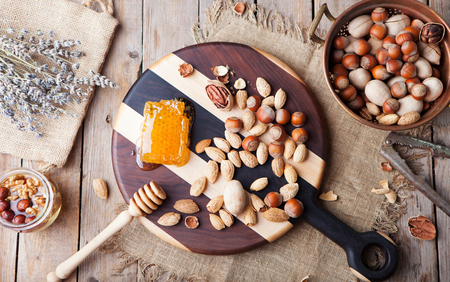 Assortment of nuts and honey with lavender flowers on a wooden rustic cutting boardの写真素材