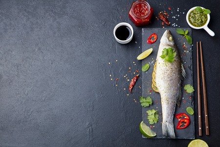 Roasted fish with sauces, fresh herbs and lime on a black slate board. Top view. Copy space.