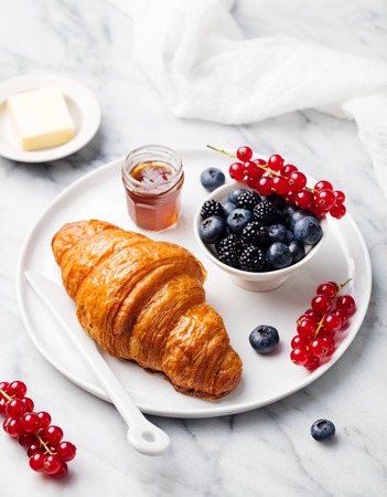 Croissant with fresh berries, chocolate spread and butter with cup of coffee on a marble texture background. Top viewの写真素材