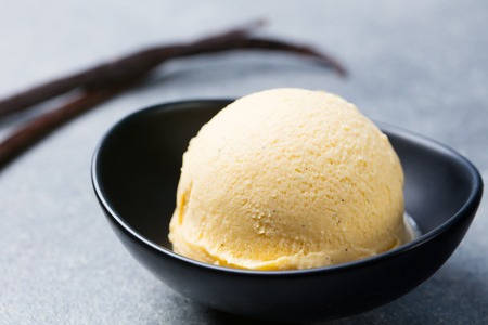 Vanilla, caramel ice cream in black bowl with vanilla pods. Organic product on a grey stone background.の写真素材