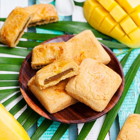 Mango cookies in wooden bowl on colorful wooden background with palm leaf.の写真素材