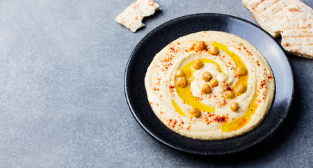 Hummus, chickpea dip, with spices in a black plate on grey stone background. Top viewの写真素材