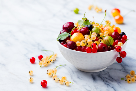 Assortment of fresh berries in white bowl. Marble background. Copy space.の写真素材