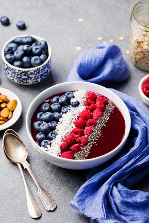 Smoothie bowl with fresh raspberry, blueberry, coconut flakes and chia seeds. Grey stone backgroundの写真素材
