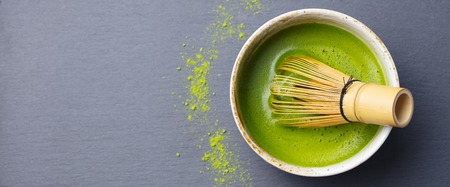 Matcha green tea cooking process in a bowl with bamboo whisk. Black slate background. Top viewの写真素材