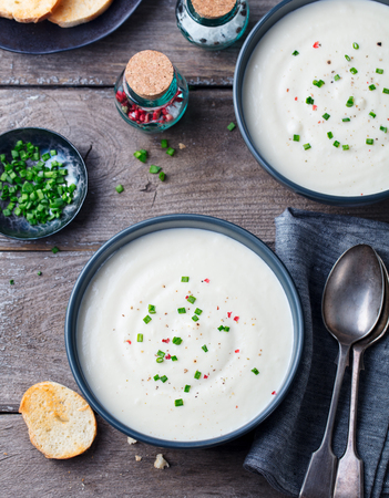 Cauliflower, potato cream soup with green onion in black bowl on wooden background. Top viewの写真素材