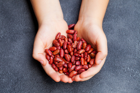 Red kidney beans in kids hands. Grey stone background. Top view.の写真素材