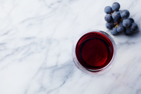 Red wine in glass with fresh grape on marble table background. Top view. Copy space.の写真素材