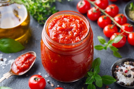 Traditional tomato sauce in a glass jar with fresh herbs, tomatoes and olive oil.の写真素材