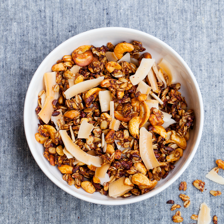 Healthy breakfast. Fresh granola, muesli with coconut, banana and nuts in a white bowl on grey textileの写真素材