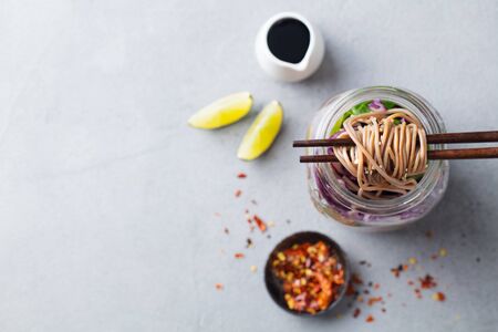 Noodles soba salad, soup with vegetables, tofu and chicken in jars. Grey background. Top view. Copy space.の写真素材