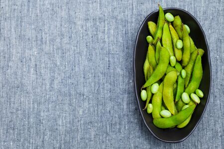 Fresh edamame green beans in black bowl. Grey textile background. Top view. Copy space.の写真素材