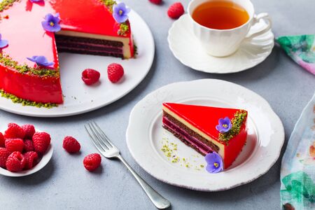 Raspberry layerd cake decorated with violet flowers and tea cup. Grey stone background.の写真素材