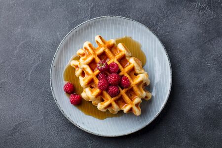 Belgian waffles with maple syrup and fresh raspberry. Grey slate background. Top view.の写真素材