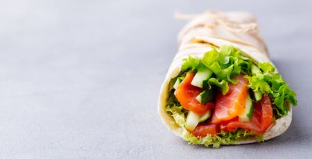 Wrap sandwich, roll with fish salmon and vegetables. Grey background. Close up.