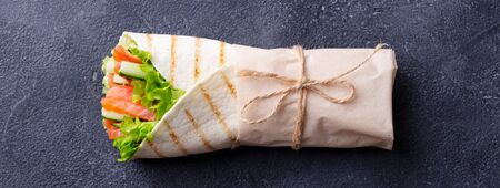 Wrap sandwich, roll with fish salmon and vegetables. Dark background. Top view.