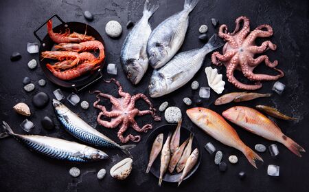 Fresh fish and seafood assortment on black slate background. Top view.