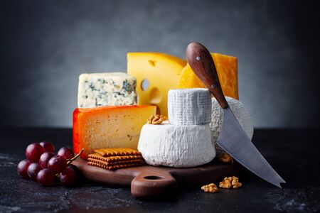 Cheese assortment: blue cheese, hard cheese, soft cheese on a cutting board. Slate black background....