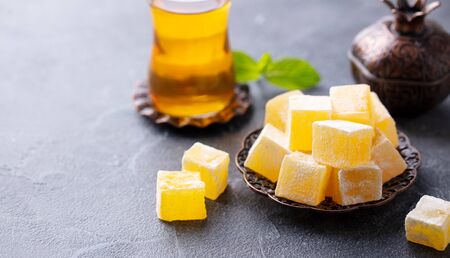 Turkish delight on a copper plate with glass of tea. Grey stone background. Copy space.の写真素材