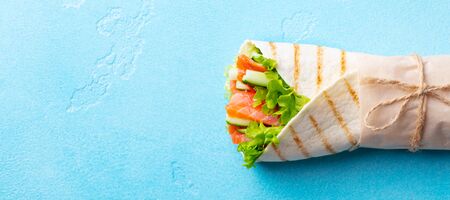 Wrap sandwich, roll with fish salmon and vegetables. Blue background. Copy space. Top view.
