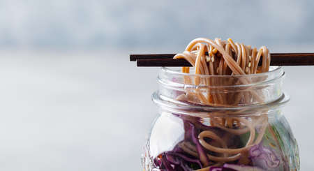 Noodles soba salad, soup with vegetables, tofu and chicken in jars. Grey background. Close up.の写真素材