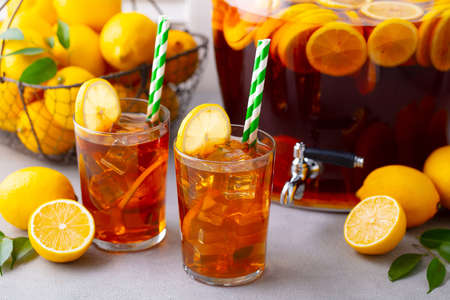 Ice tea, lemonade in glass and beverage dispenser with fresh lemons. Grey background. Close up.の写真素材
