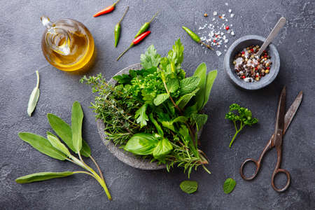 Fresh herbs in stone bowl with olive oil and spices. Grey background. Top view.の写真素材