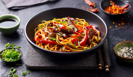 Stir fry noodles with vegetables and beef in black bowl. Slate background. Close up.の写真素材