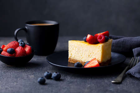 Cheesecake dessrt with fresh berries and cup of coffee. Dark background.