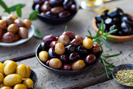 Assortment of fresh olives on a plate with olive tree brunches. Wooden background. Close up.の写真素材