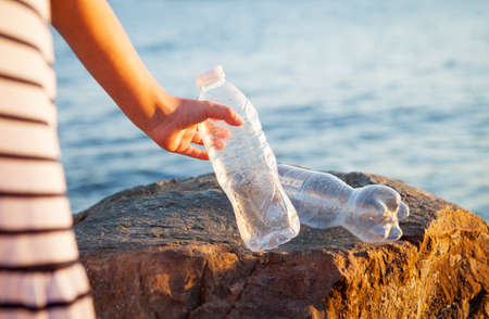 Young girl cleans beach, gathering plastic bottles. Close up.