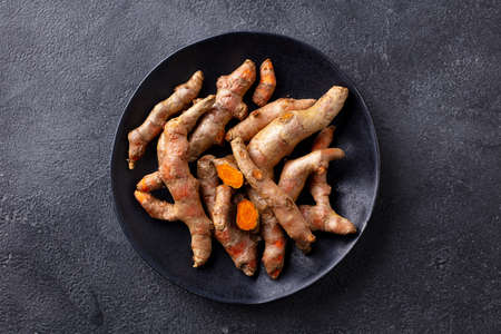 Fresh turmeric, curcumin, tumeric roots on a black plate. Superfood product. Dark background. Close...