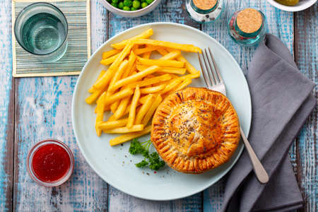 Meat pie with french fries on a white plate. Wooden background. Close up. Top view.