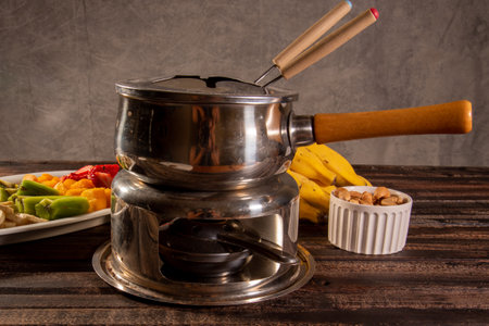 chocolate fondue accompanied by tropical fruits on wooden table and dark backgroundの写真素材