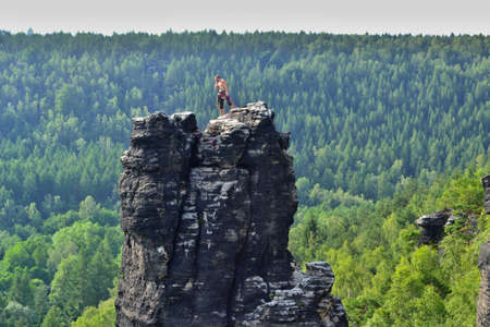 Ostrov, Czech Republic - MAY 25, 2019: Climber is standing on top of a rock looking down to see his friend climbing. Beautiful sunny day, sandstone towers. |のeditorial素材