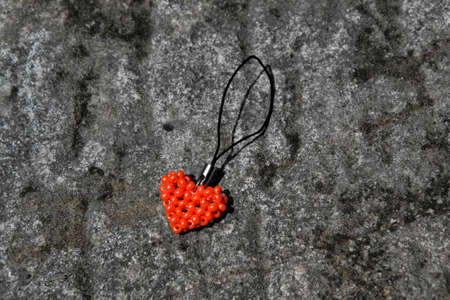 Orange heart from beads on black cord. Pendant lying on stone surface.の写真素材