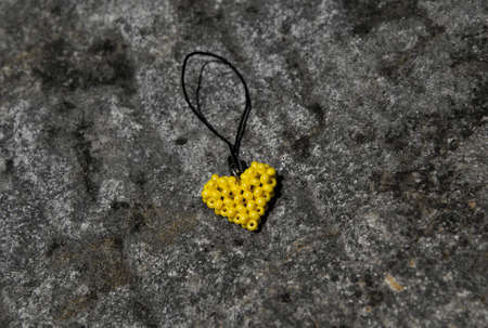 Yellow heart from beads on black cord. Pendant lying on stone surface.の写真素材