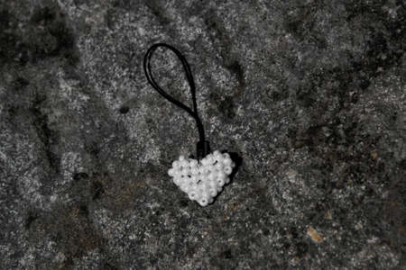 White heart from beads on black cord. Pendant lying on stone surface.