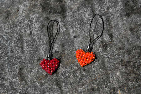 Orange and red heart from beads on black cord. Pendant lying on stone surface.