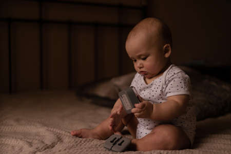 Infant boy sits in the bed and plays with toy in cozy room. Light from window. High quality photo.の写真素材