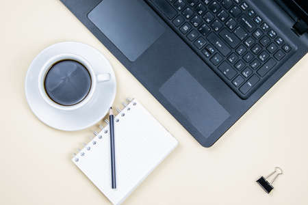 A cup of black aromatic coffee with a notebook and a laptop. Light yellow background