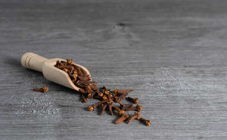 A wooden scoop with dried cloves on a dark wooden tableの写真素材